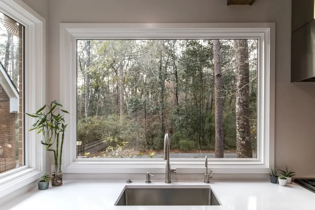 A large farmhouse single farm house sink with a massive picture window with a view of the wooded lot yard.