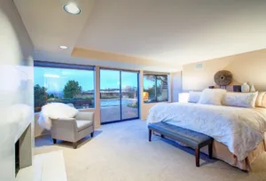 Lovely bedroom design in soft beige and cream tones boasts queen size bed with tufted bench , traditional fireplace and glass sliding doors to amazing poolside patio space. Northwest, USA