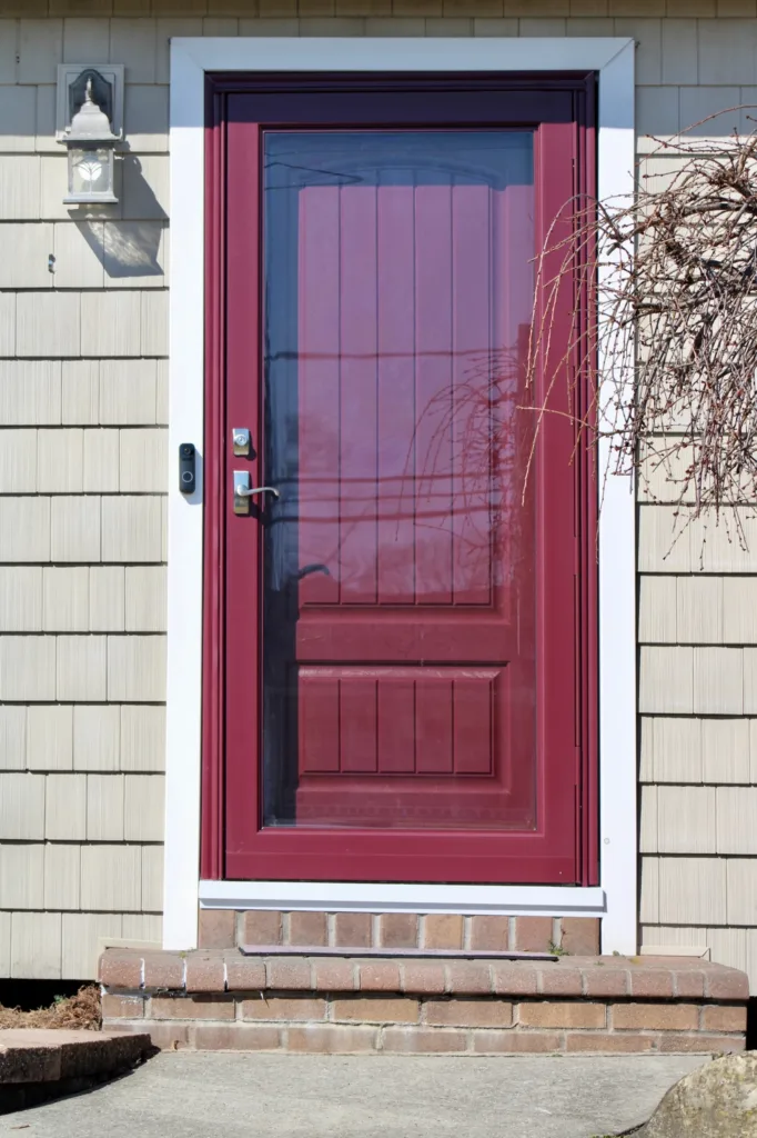 The close up image of a newly installed front door on a home. The door is a deep red, berry color. There is a matching storm door.