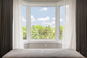 Bay window with drapes, curtains and view of trees under summer sky