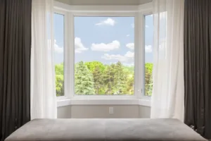 Bay window with drapes, curtains and view of trees under summer sky