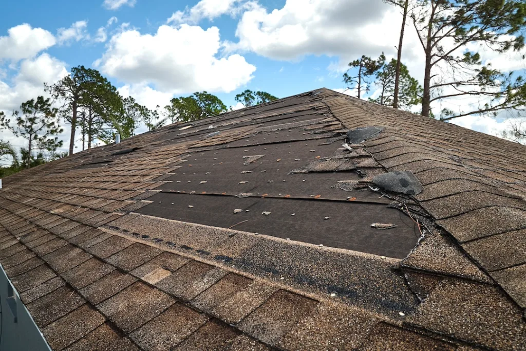 Wind damaged house roof with missing asphalt shingles