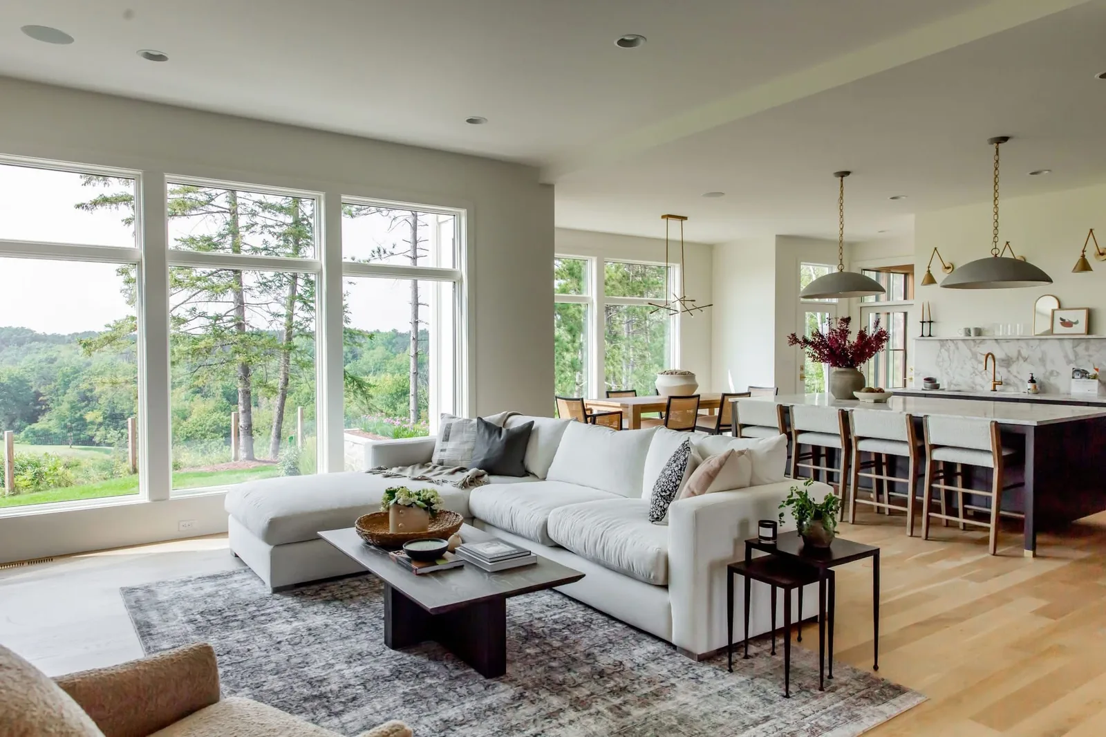 Bright living room with a white sectional, large white-framed windows, and an open kitchen.