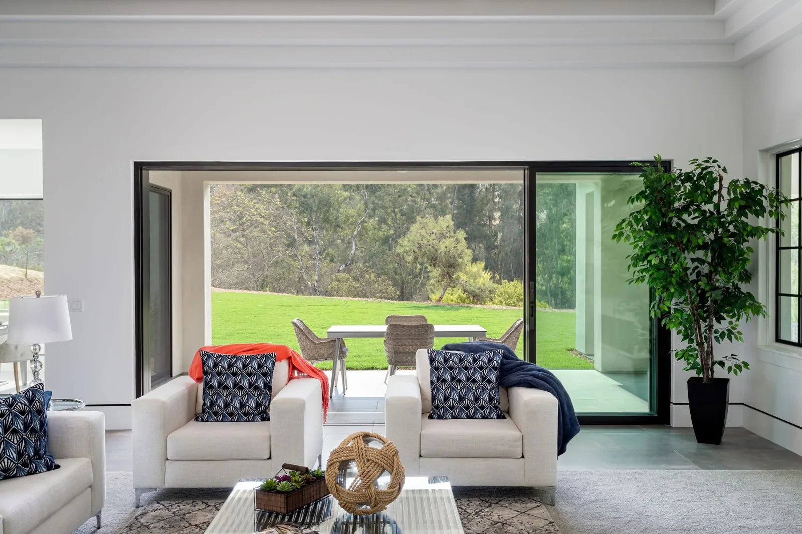 Living room with white armchairs and wide black-framed glass doors opening onto a patio.