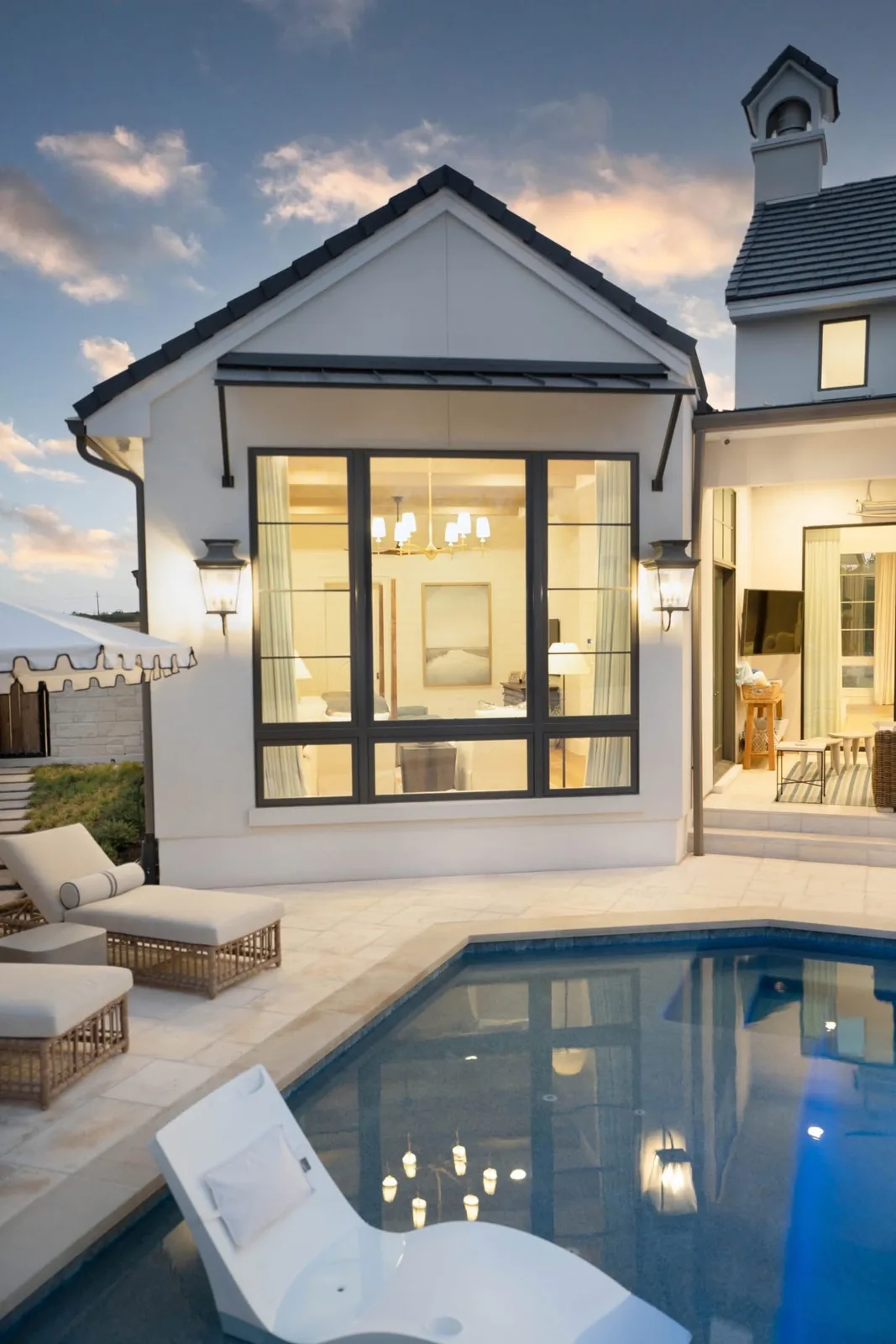 White home with large black-framed windows beside a swimming pool at dusk.