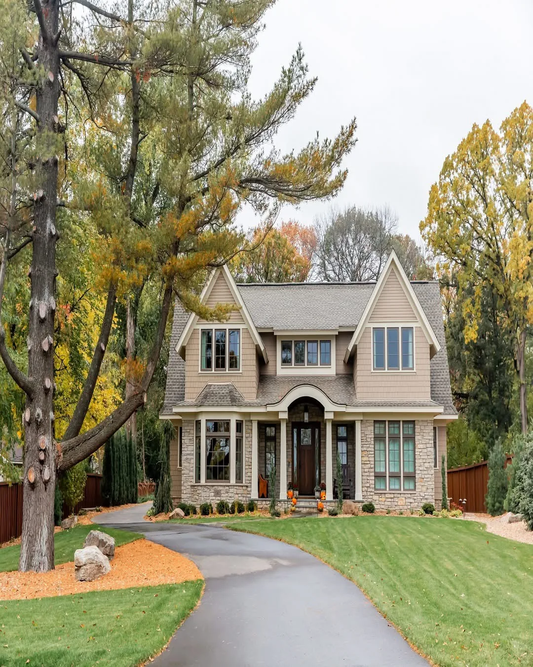 Shingle-sided house with tall windows, twin front gables, and a curved driveway surrounded by trees.